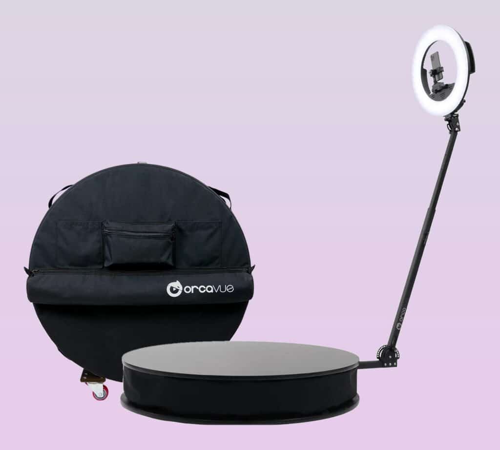 OrcaVue Air 360 photo booth with ring light and phone mount, next to its canvas cover on a dolly